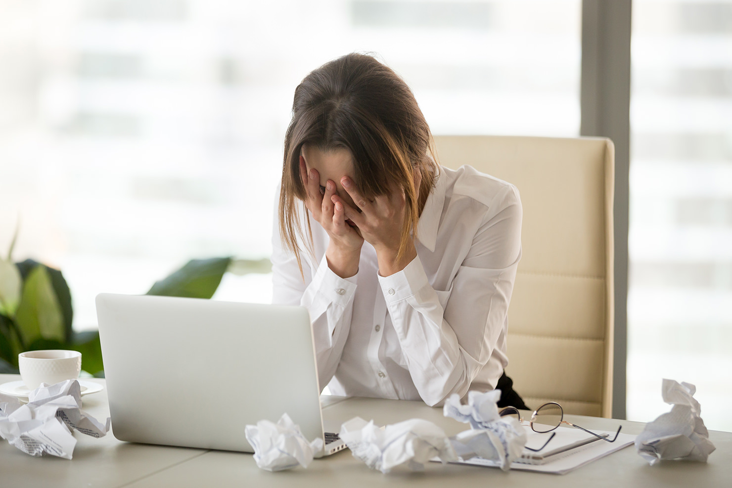 A woman stressed at her desk with crumpled paper.